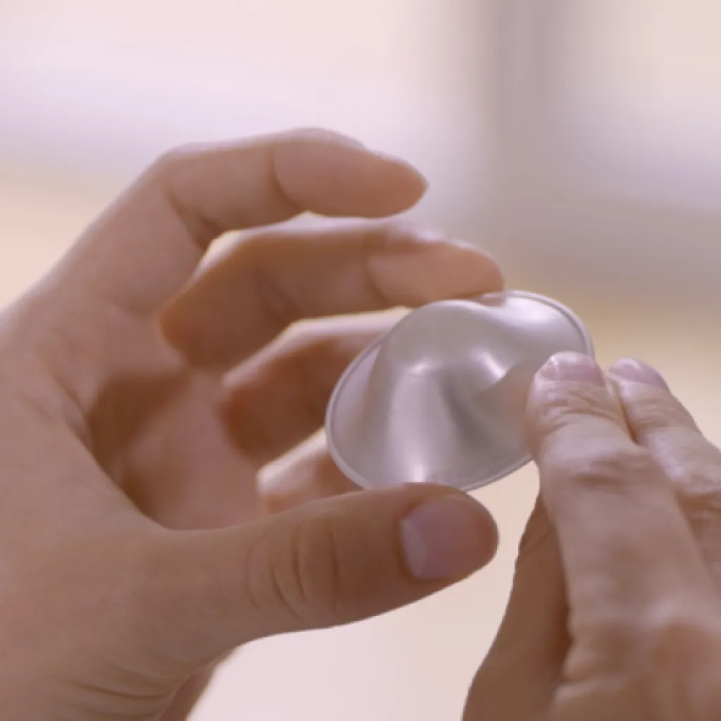 Due mani che tengono una coppetta in argento Silverette®: il dispositivo per la cura del capezzolo e l’aiuto contro le ragadi durante l'allattamento.