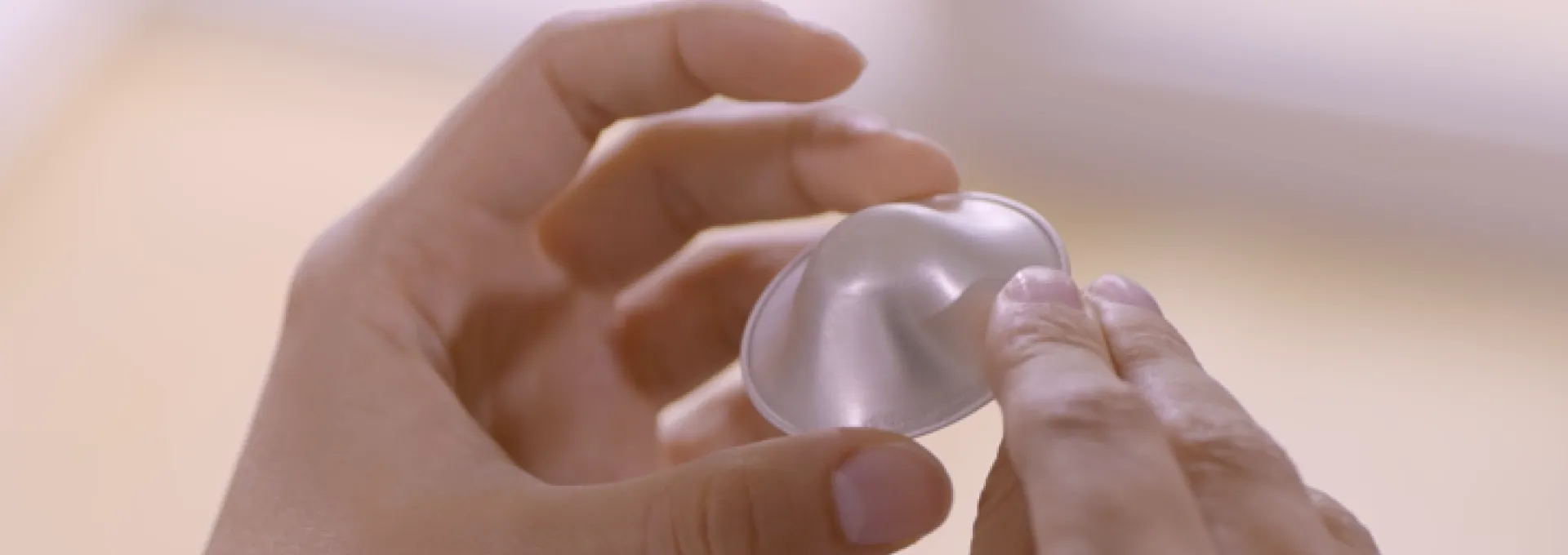 Due mani che tengono una coppetta in argento Silverette®: il dispositivo per la cura del capezzolo e l’aiuto contro le ragadi durante l'allattamento.