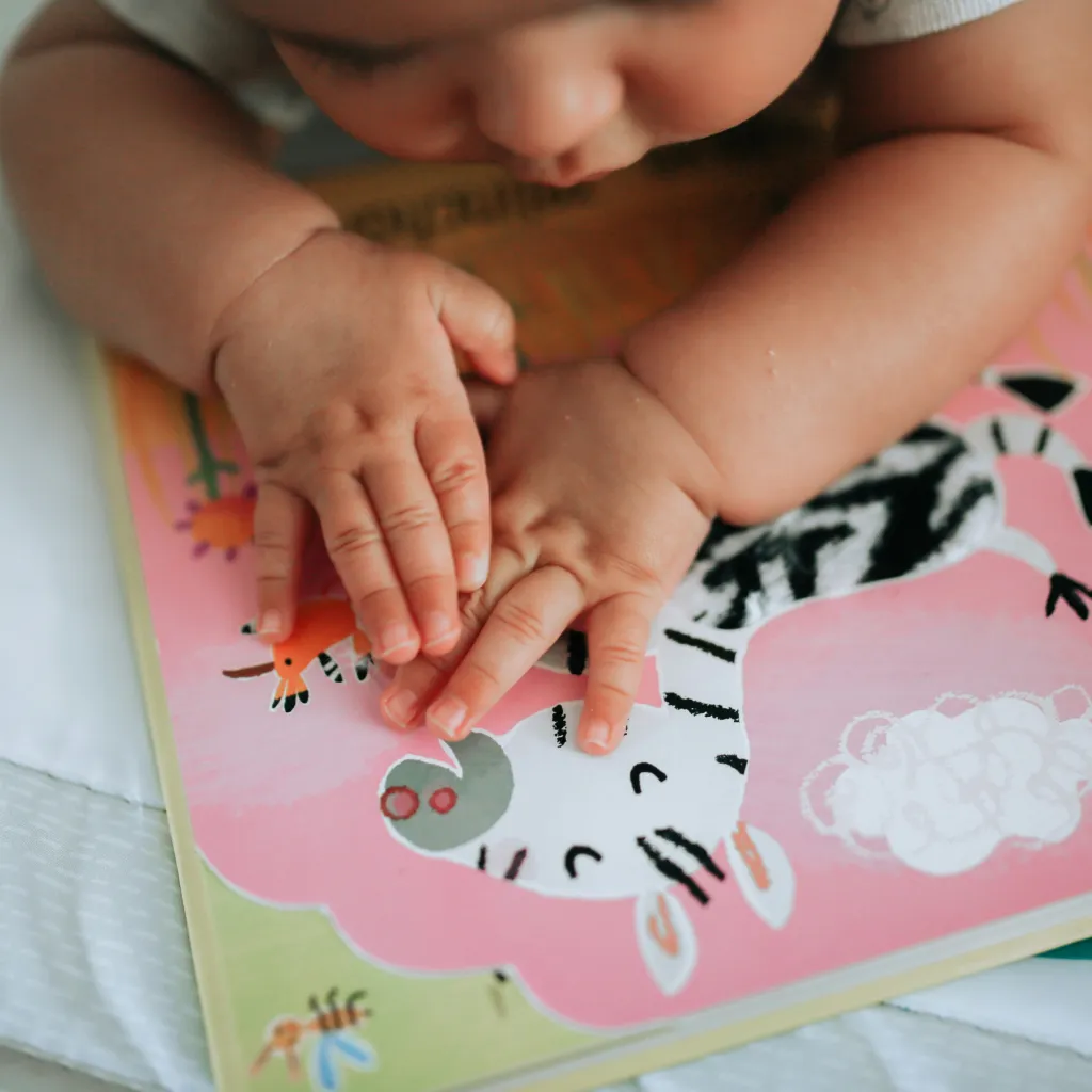 Neonato sdraiato a pancia in giù che sta guardando un libro sensoriale di immagini tattili e colorate